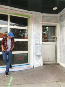 Person standing in front of a building's window with primer on the walls and to the left of a white door.