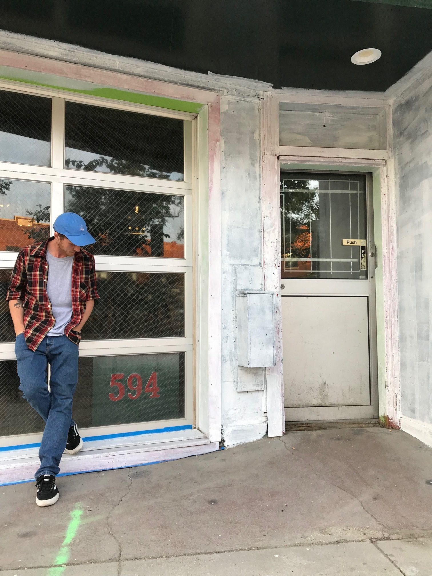 Person standing in front of a building's window with primer on the walls and to the left of a white door.