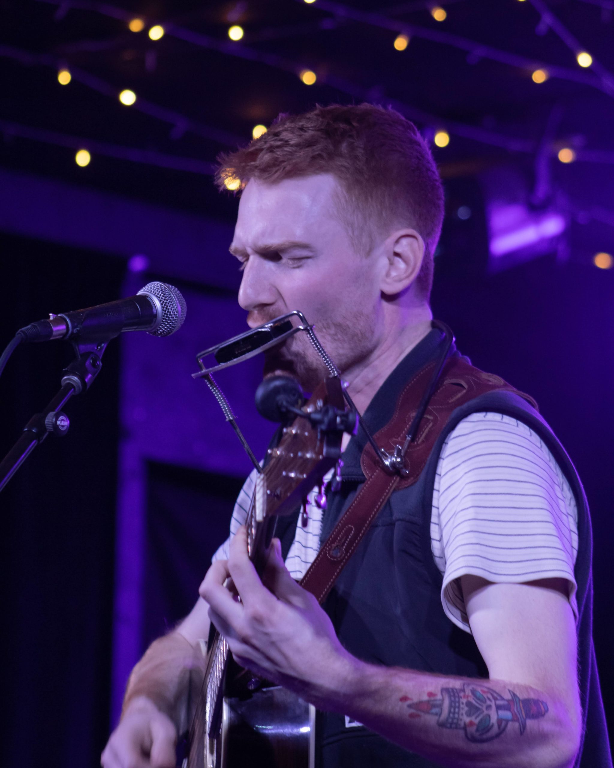 Stephen Hodges performing on stage with a guitar and a harmonica.