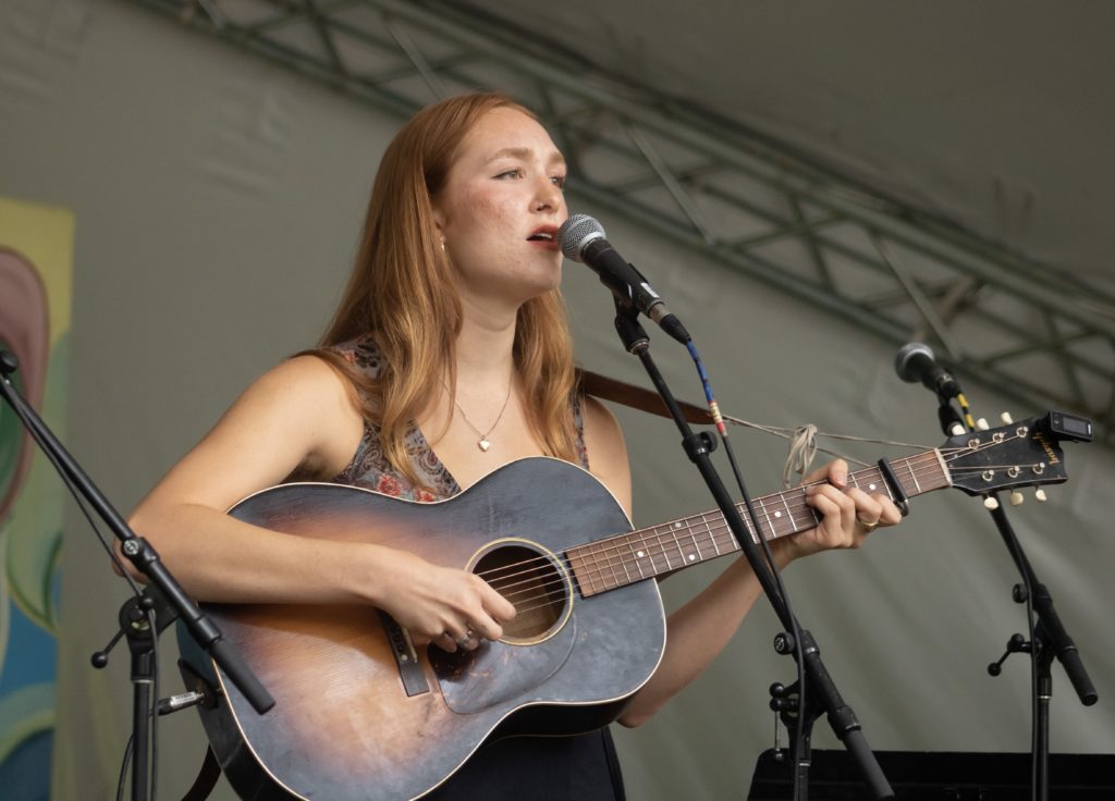 Bella White sings into mic while playing electric acoustic guitar at Winnipeg Folk Fest.