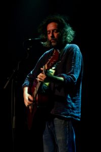 Person standing, playing guitar on stage