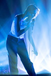 Lead singer performing on stage with blue light and smoke behind.