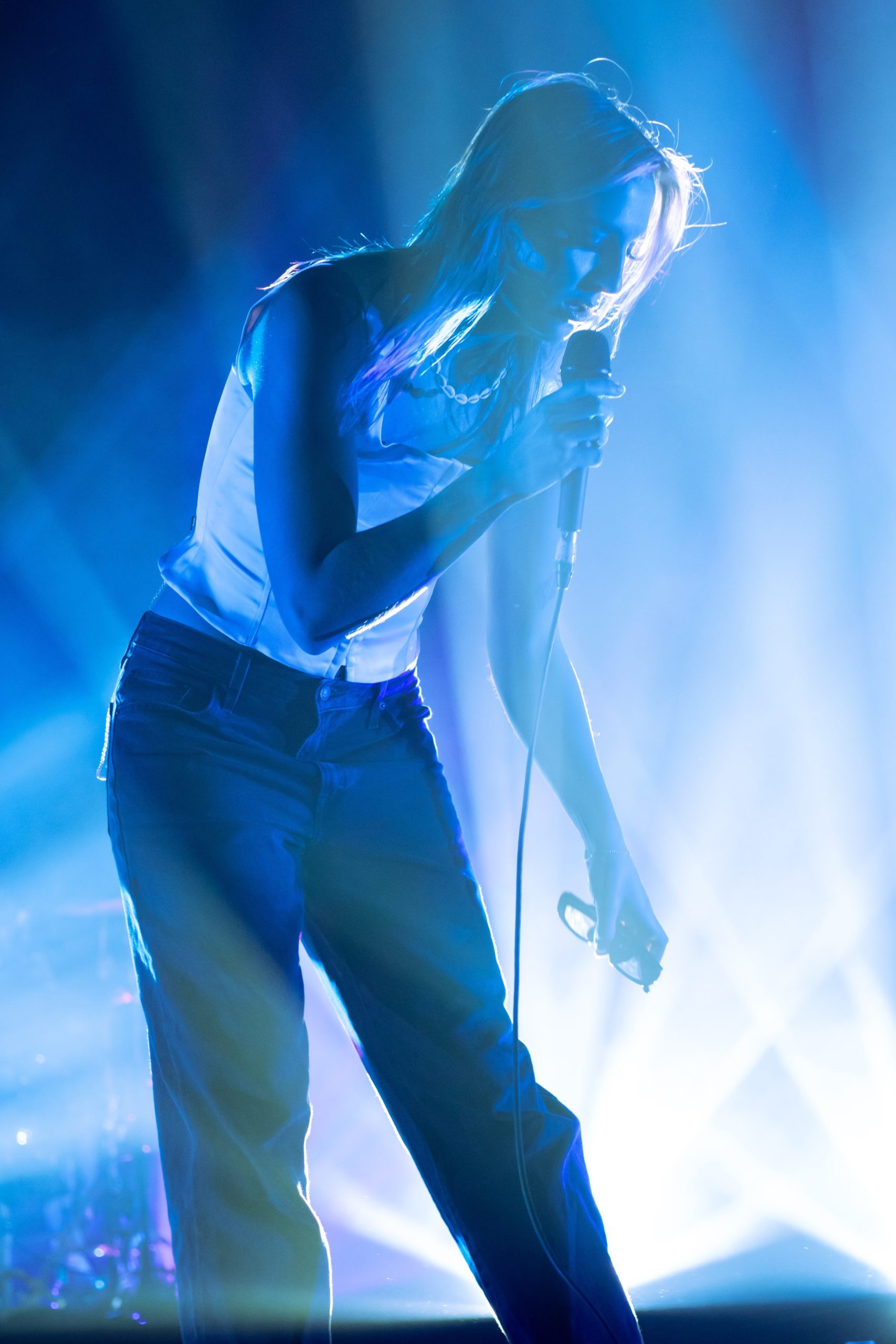 Lead singer performing on stage with blue light and smoke behind.