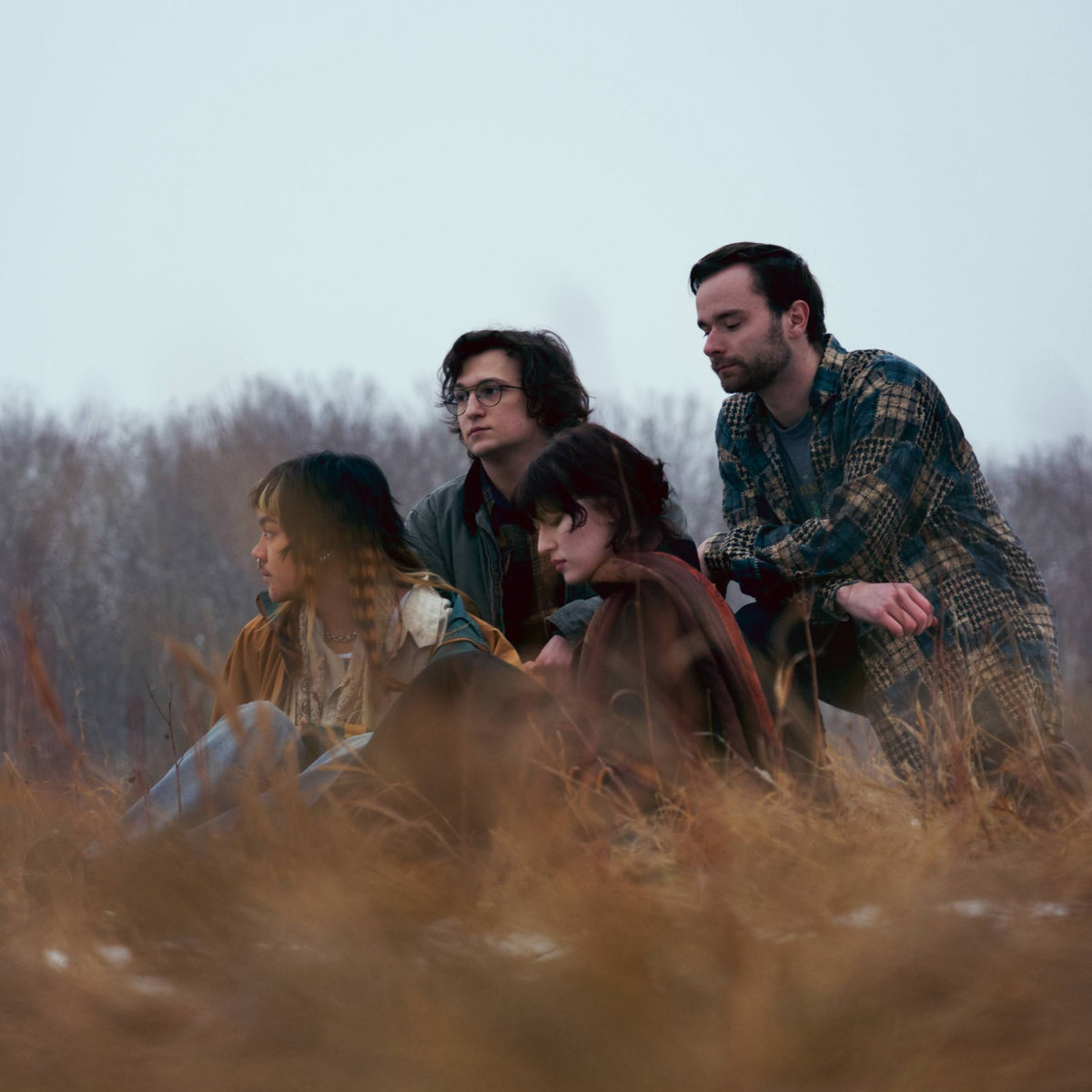Four people sitting in a field on a gloomy day.