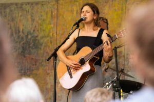 Helena Ross performing on stage with a guitar in daylight.