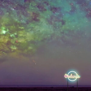 Green multi-coloured evening sky. A neon light-up sign on a flat landscape reads "Orelands" in orange with a blue circle surrounding it in the bottom right corner of the image.